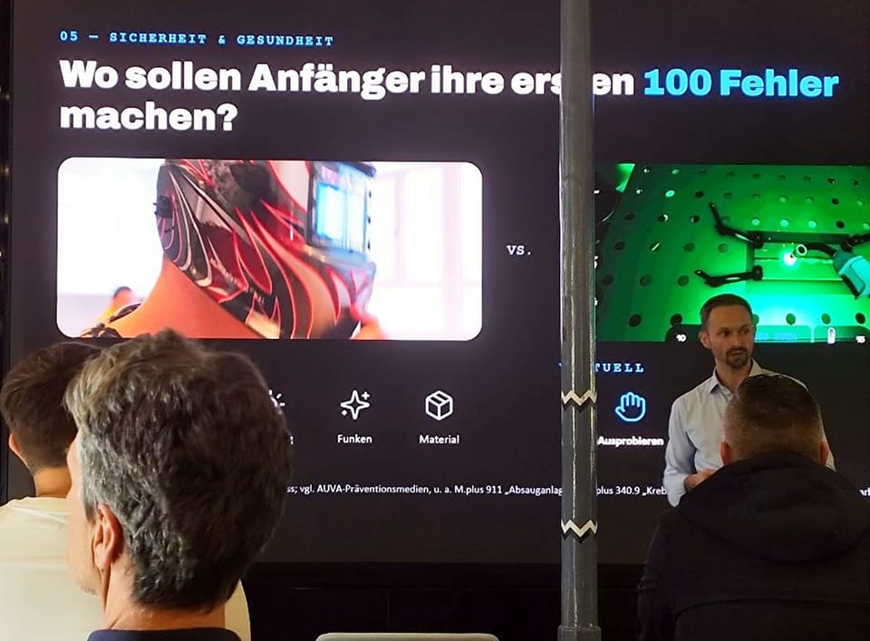 Vortragender im hellblauen Hemd vor einer Folie, die echtes und virtuelles Schweißtraining vergleicht