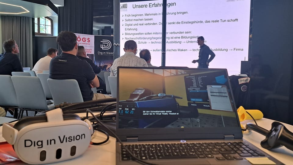 VR-Brille mit Dig-in-Vision-Logo und Laptop mit Schweißsimulator auf einem Tisch, dahinter Publikum und ein Vortragender vor der Folie „Unsere Erfahrungen“