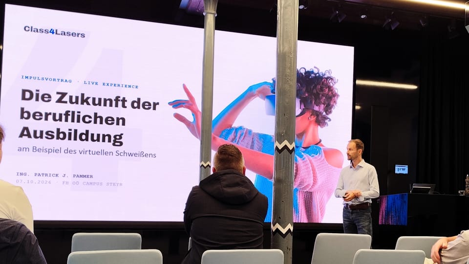 Vortragender neben großer Leinwand mit dem Titel „Die Zukunft der beruflichen Ausbildung“, im Vordergrund Publikum
