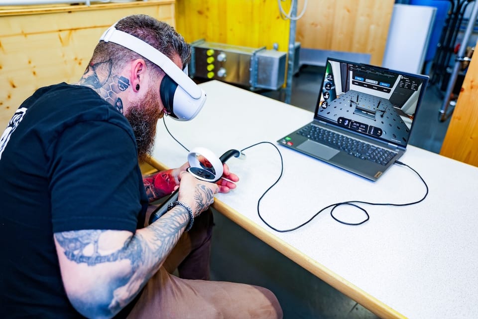 Tätowierter Mann mit VR-Brille und Controller vor einem Laptop